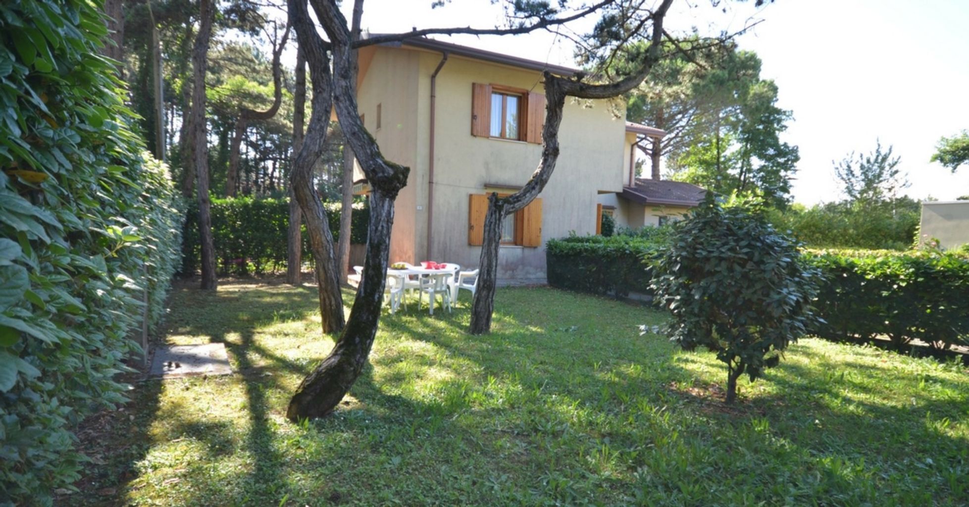 Una casa con jardín, mesa y sillas, y un árbol pequeño.