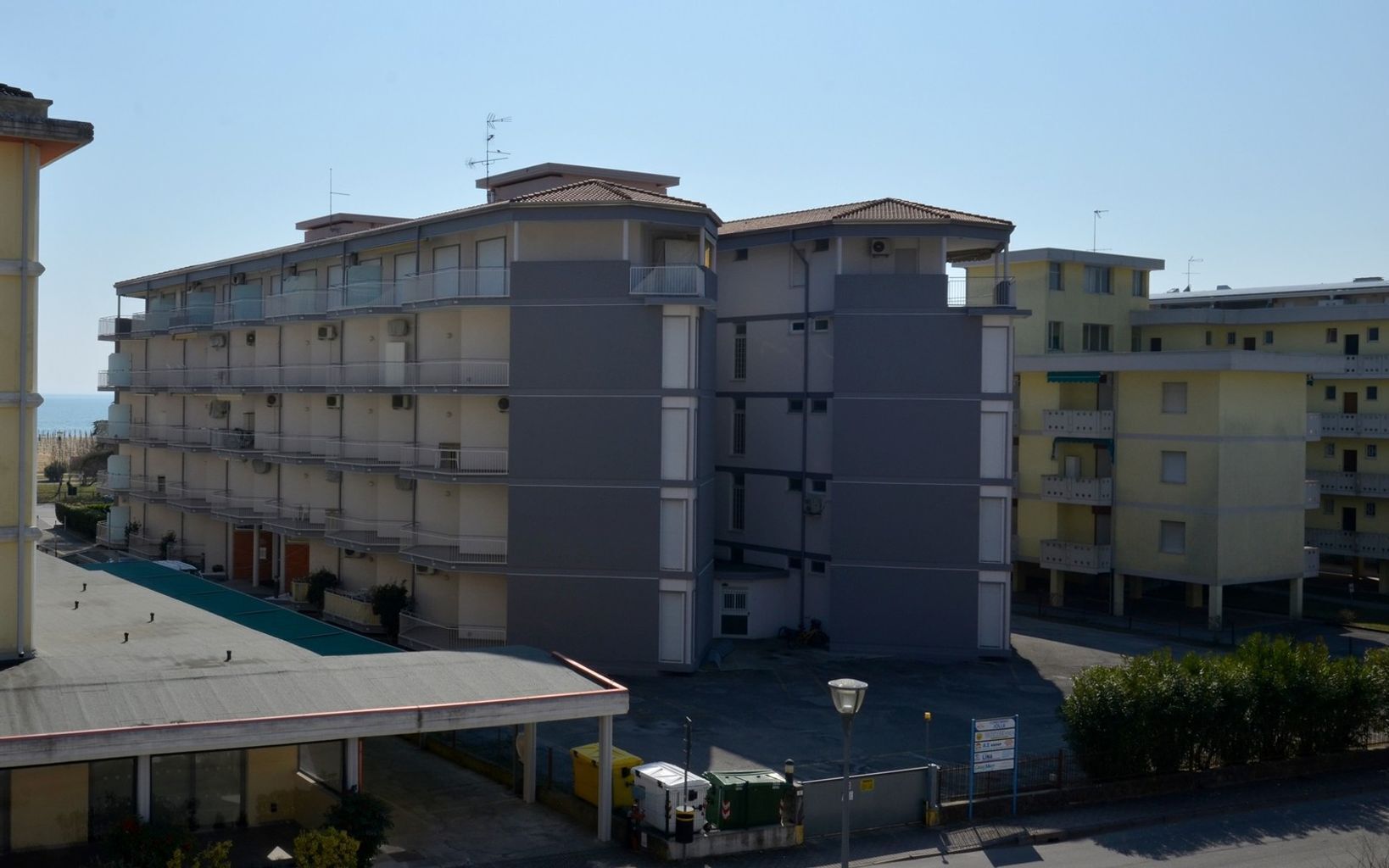 Un hotel de varios pisos con balcones, zona de estacionamiento techada y vistas al mar.