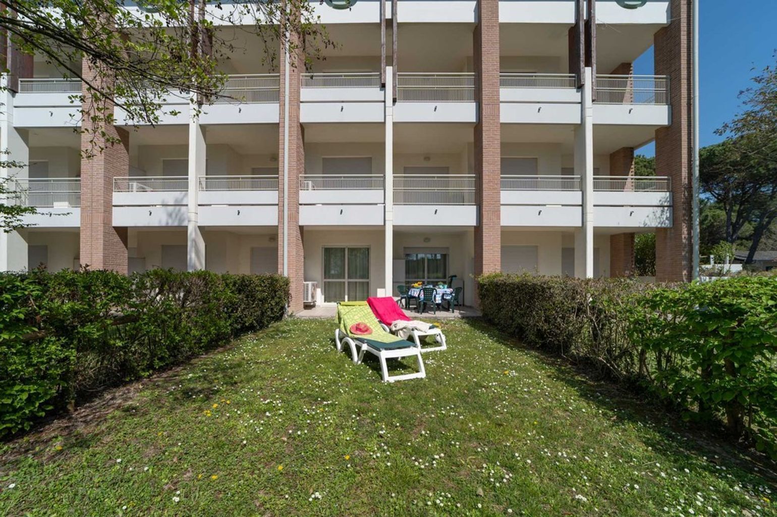 A multi-story building with a central courtyard, a covered seating area with a table and chairs, and a small garden area with a lawn and a few flowers.