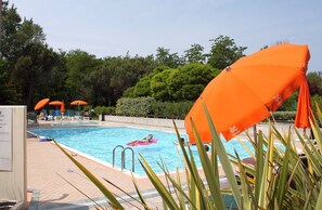 A swimming pool with orange umbrellas, lounge chairs, and a tiled deck. - Great flat with private garden in Bibione Pineda (Bibione)
