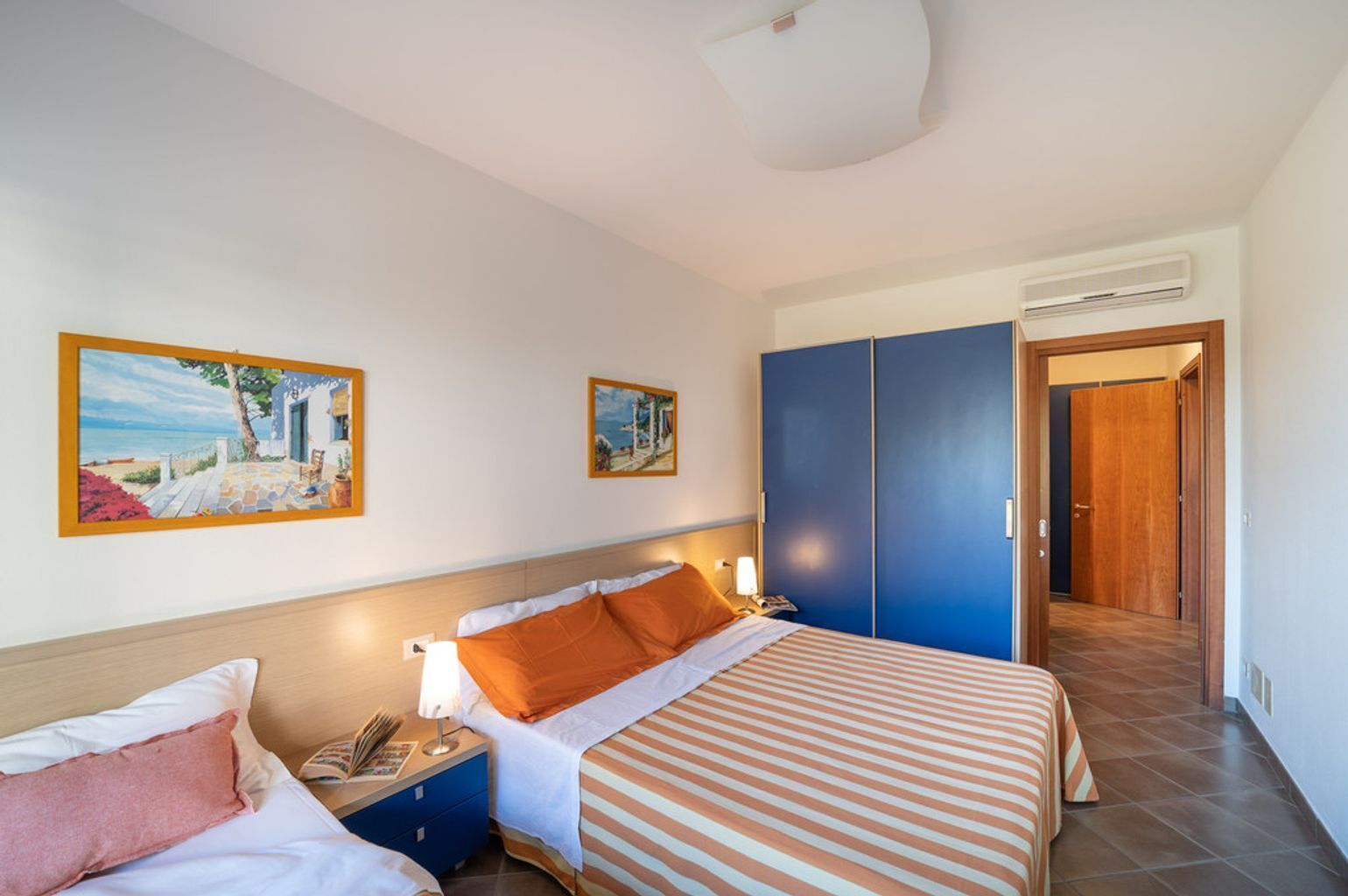 Ein Hotelzimmer mit zwei Betten, einem Schrank, einem Nachttisch und zwei Bildern an der Wand.