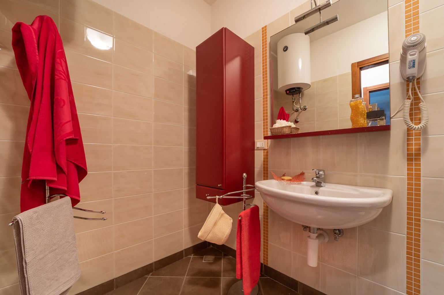Een badkamer met een wastafel, spiegel, handdoekhouder en een rode kast.