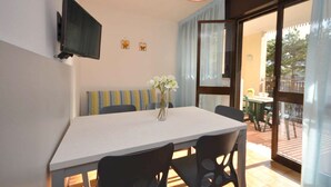 A dining area with a table, chairs, a vase with flowers, a flat-screen TV mounted on the wall, and a sliding glass door leading to an outdoor patio.