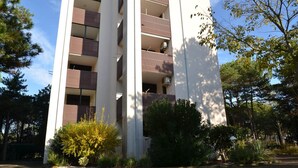 A multi-story building with balconies, surrounded by trees and shrubs.