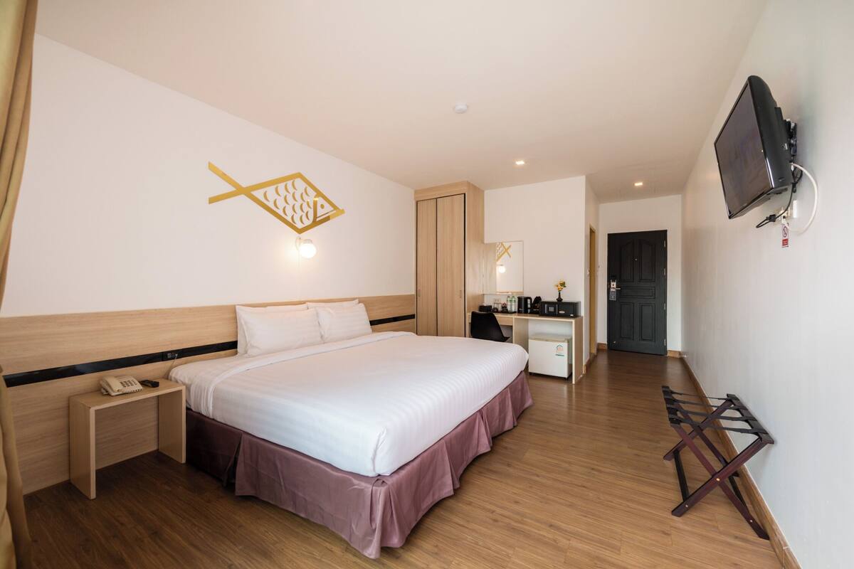 Ein Hotelzimmer mit Bett, Nachttisch, Schreibtisch, Stuhl, Fernseher und einem an der Wand befestigten Handtuchhalter.