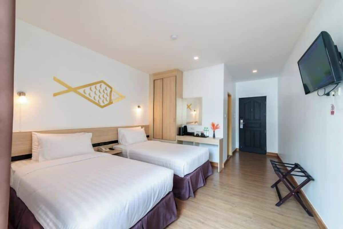 Ein Hotelzimmer mit zwei Betten, einem Fernseher, einem Schreibtisch mit Spiegel und Holzboden.