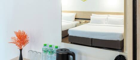 A hotel room with a bed, a bedside table with a vase, water bottles, a kettle, and a hair dryer bag.