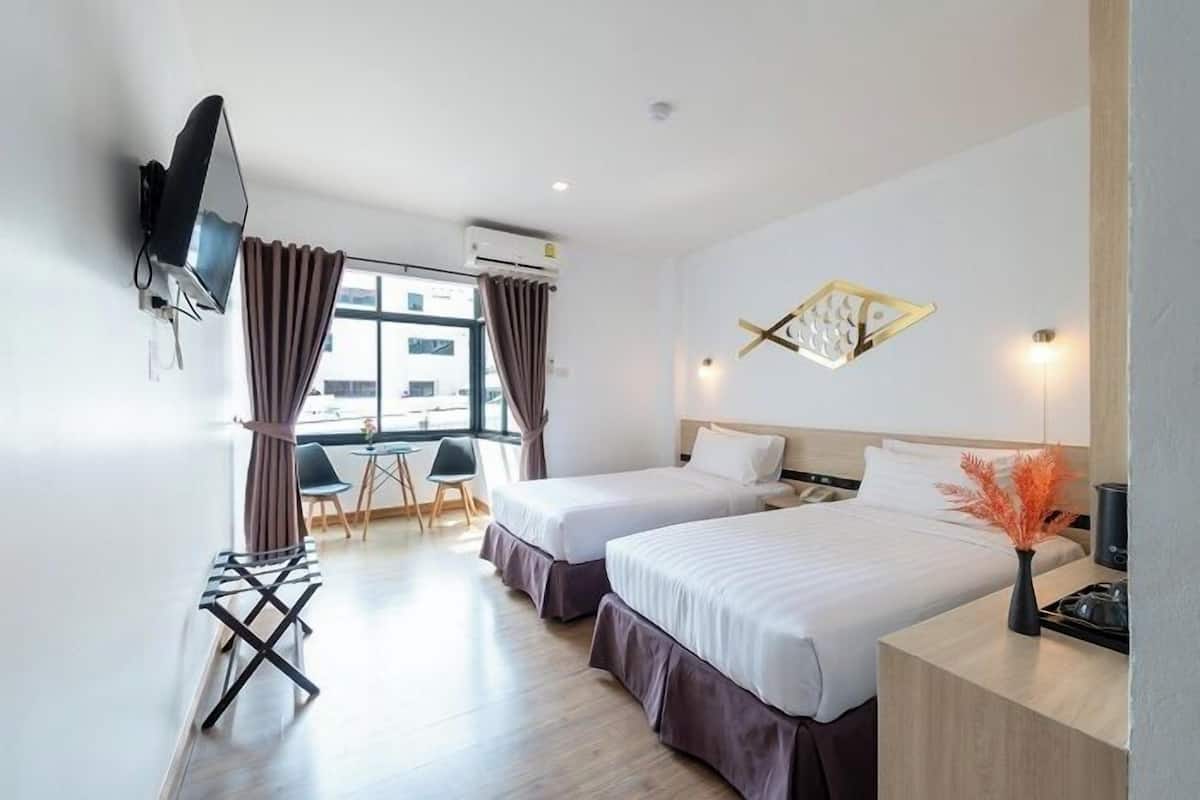 Ein Hotelzimmer mit zwei Betten, einem an der Wand befestigten Fernseher, einem Schreibtisch mit einer Vase und einem Fenster mit Vorhängen.