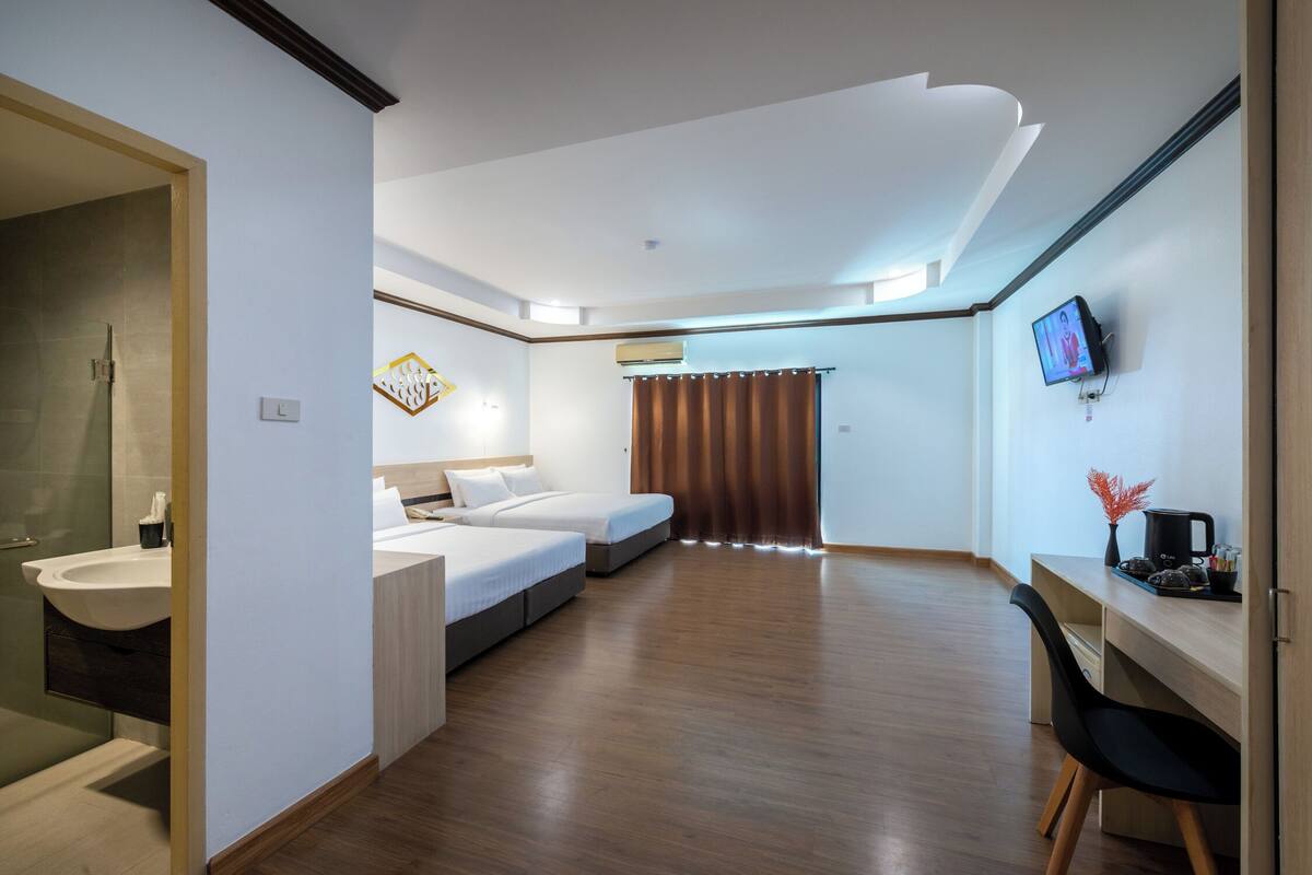 Ein Hotelzimmer mit Holzboden, einem Bett, einem Schreibtisch mit Stuhl, einem Fernseher und einem Badezimmer mit Waschbecken.