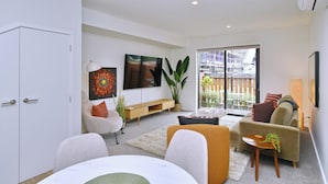 A modern living room with a sofa, coffee table, and TV. There is a sliding glass door leading to a balcony. - Modern City Apartment with Style and Comfort (Christchurch)