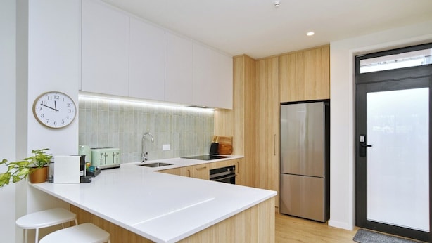 A modern kitchen with a central island, white cabinetry, a stainless steel refrigerator, and a clock on the wall. - Modern City Apartment with Style and Comfort (Christchurch)