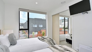 A modern hotel room with a large bed, a flat-screen TV, and a view of the cityscape through the window. - Modern City Apartment with Style and Comfort (Christchurch)