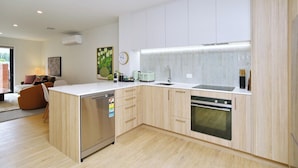 A modern kitchen with a dishwasher, oven, and a sink. There is a dining area with a couch and a coffee table. - Modern City Apartment with Style and Comfort (Christchurch)