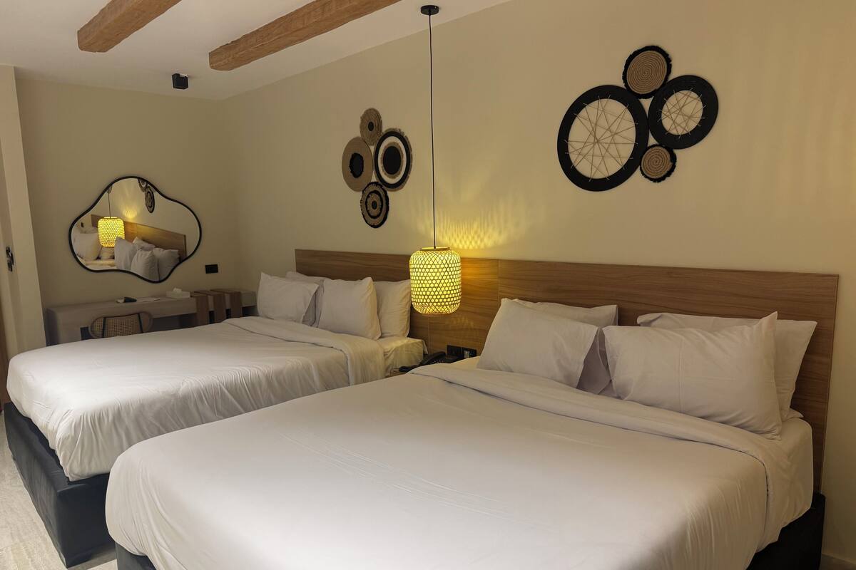 A hotel room with two beds, a wooden headboard, a wall-mounted mirror, and decorative wall art.