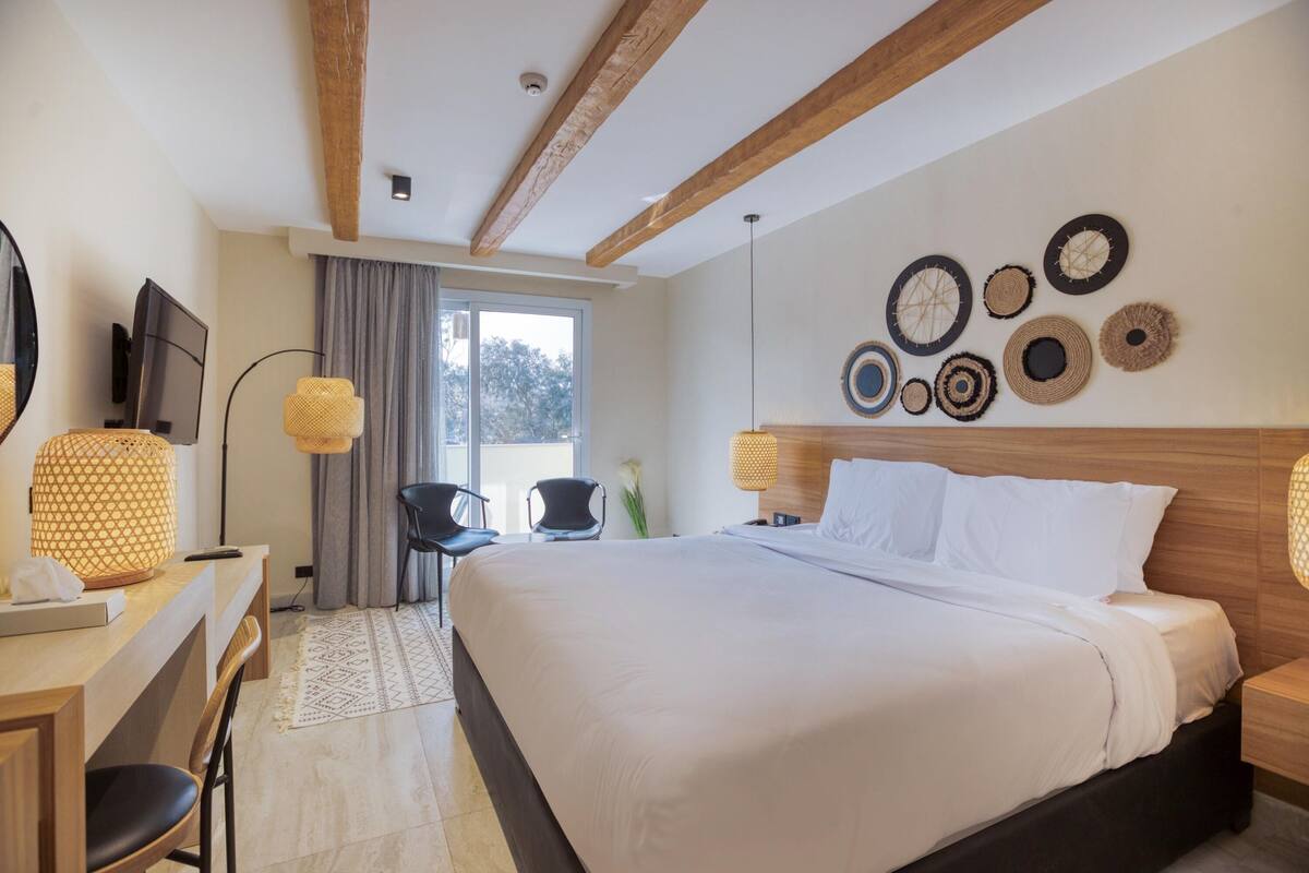 A hotel room with a large bed, a desk with a chair, a TV, and a window with curtains.