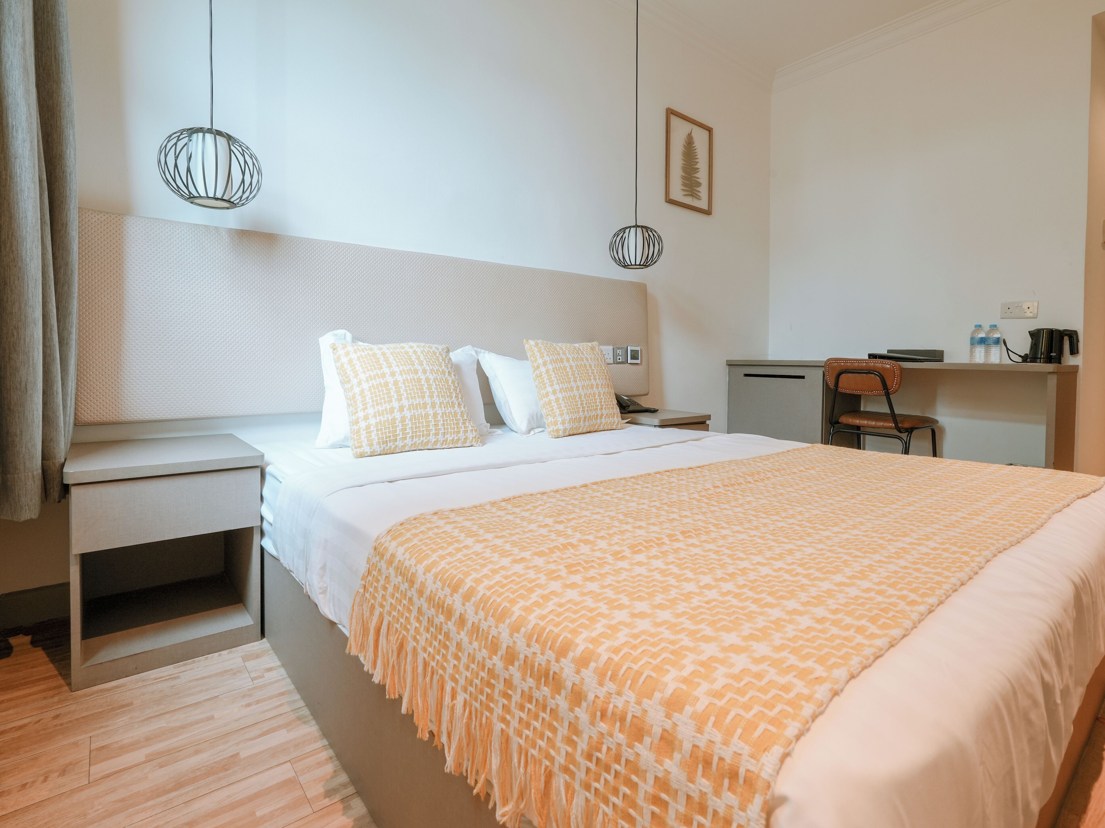 Une chambre d’hôtel comprenant un lit, une table de chevet, un bureau, une chaise et une œuvre d’art représentant une feuille, encadrée et accrochée au mur.