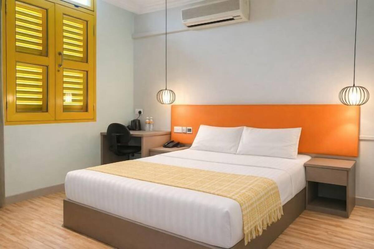 Ein Hotelzimmer mit einem Bett, zwei Nachttischen, einem Schreibtisch, einer Klimaanlage und einem Fenster mit Rollläden.
