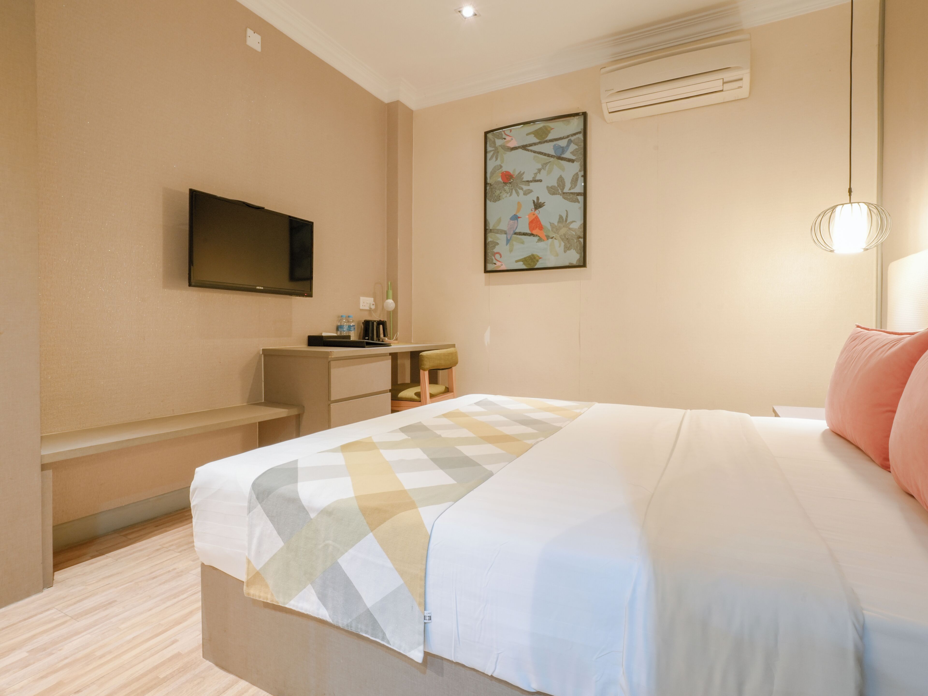Una habitación de hotel con cama, escritorio, silla, televisión y aire acondicionado.