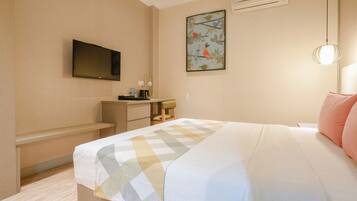 Una habitación de hotel con cama, escritorio, silla, televisión y aire acondicionado.