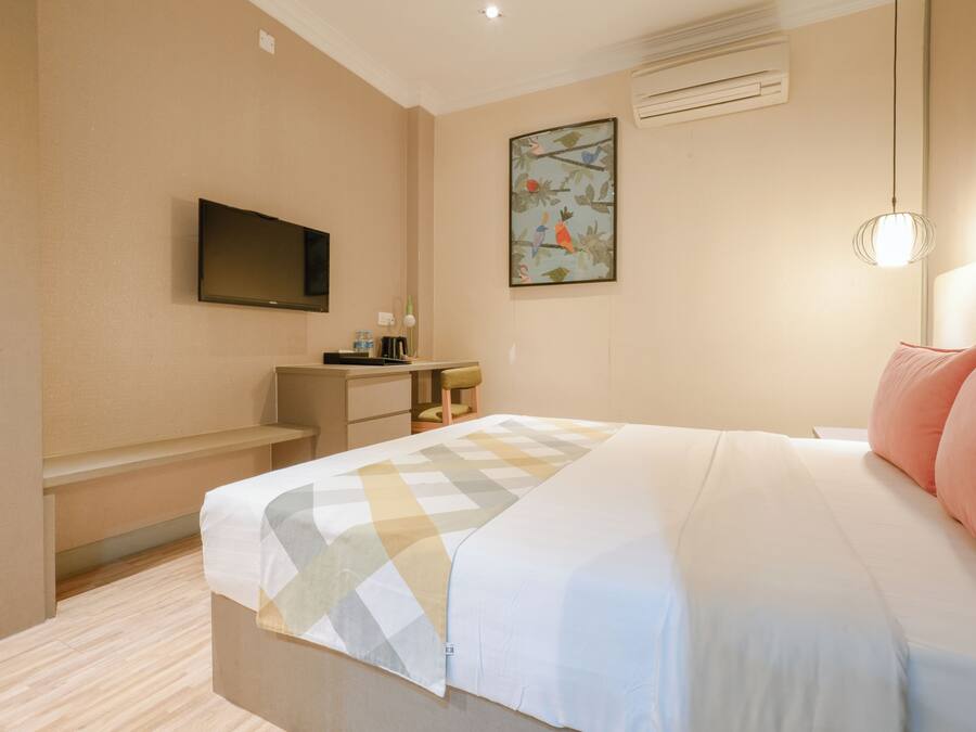 Una habitación de hotel con cama, escritorio, silla, televisión y aire acondicionado.
