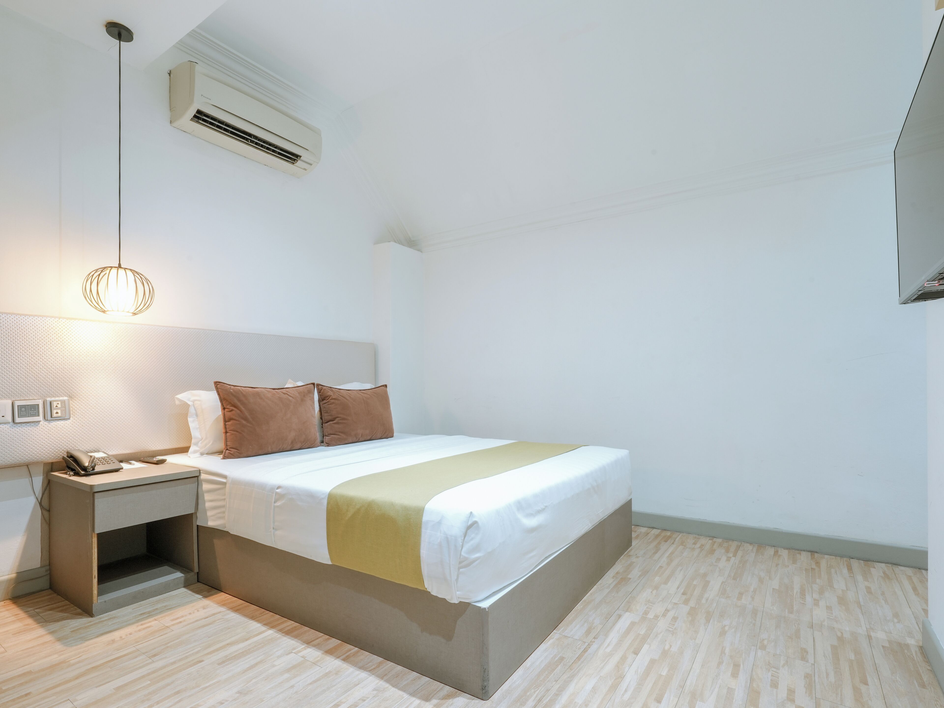Una habitación de hotel moderna con una cama bien hecha, una mesita de noche con lámpara y un equipo de aire acondicionado en la pared.