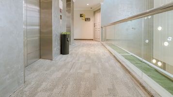 A modern hallway with a marble floor, a black trash bin with a plant, and a glass wall with hanging lights.