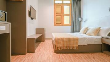 Een hotelkamer met een bed, een bureau, een stoel, een televisie en een raam met gordijnen.