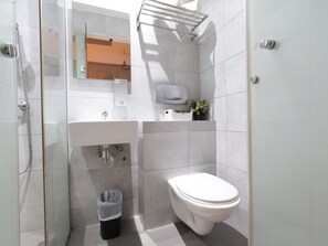 A modern bathroom with a glass-enclosed shower, a white sink, a toilet, and a small potted plant on the countertop. - A Hotel Joo Chiat Stay from 7PM to 9AM (Singapore)