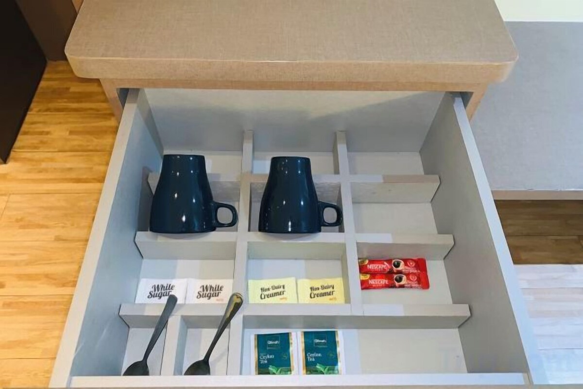 A drawer with two blue mugs, a spoon, and boxes of creamer.