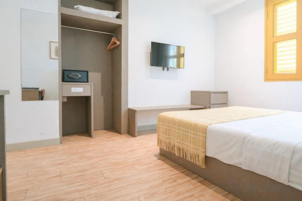 A bedroom with a bed, a desk, a television, and a wardrobe.