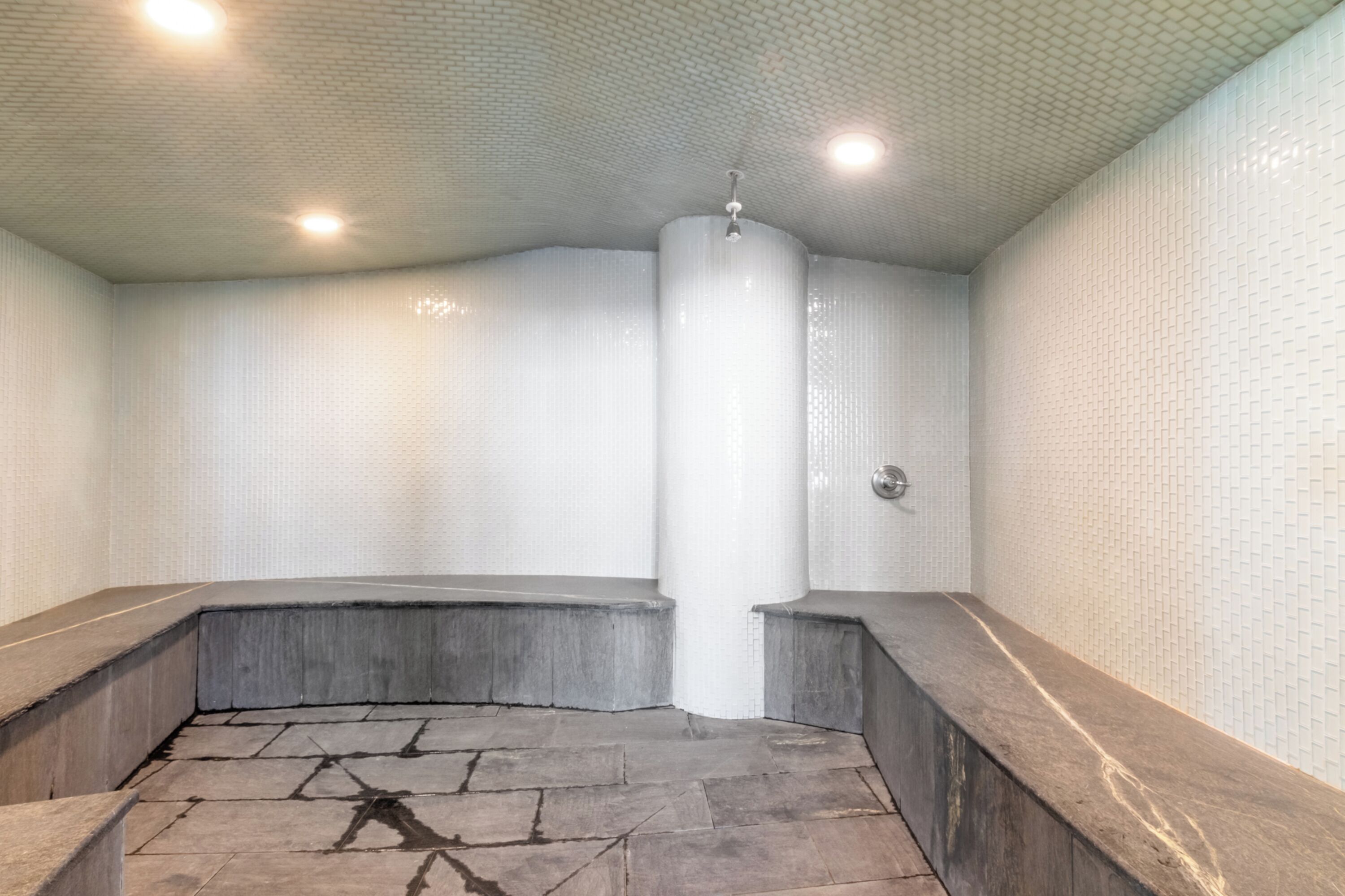 Un área de spa con suelo de piedra, paredes cubiertas de azulejos blancos y una columna central.