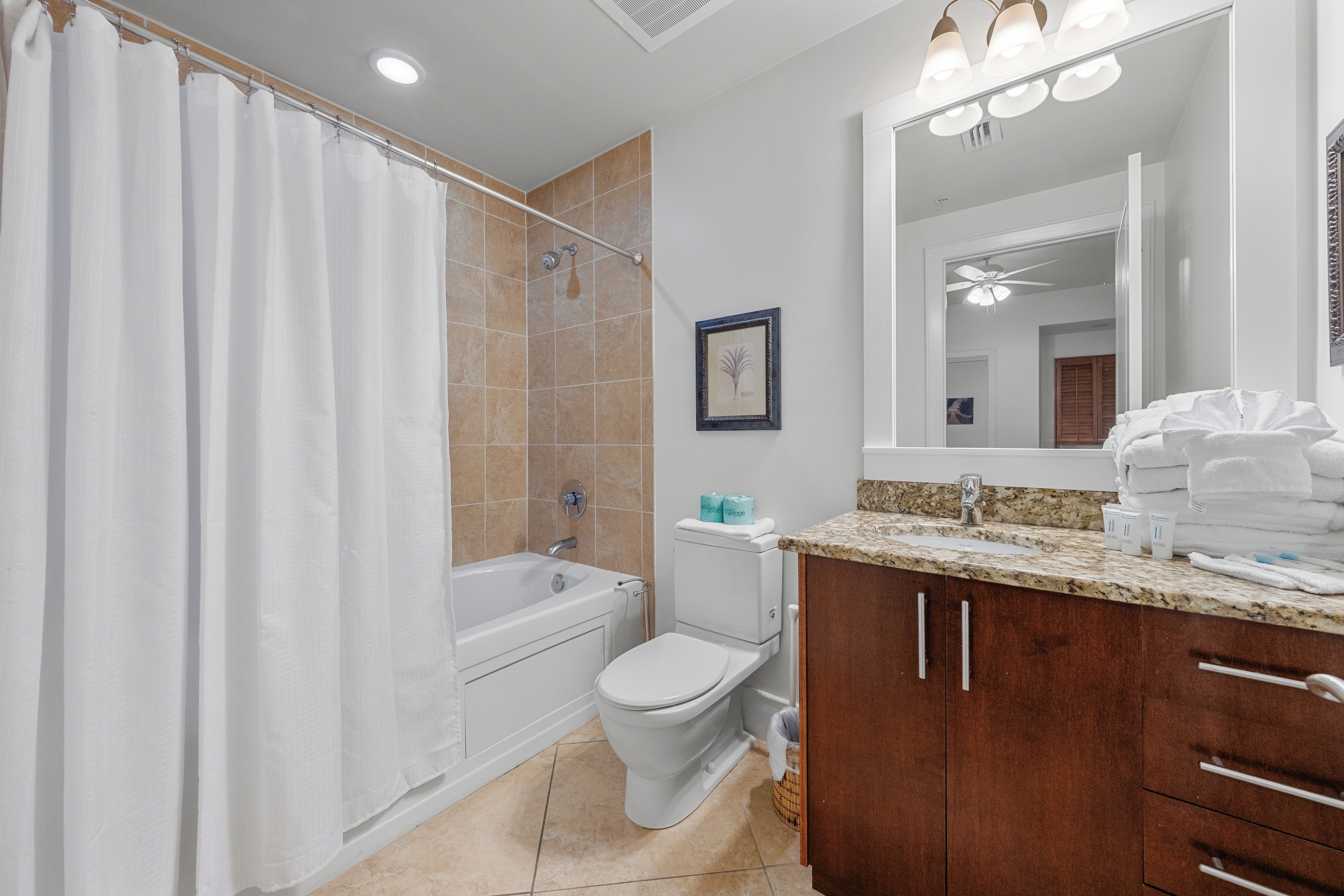 A bathroom with a bathtub, toilet, and vanity with a mirror and towel stack.