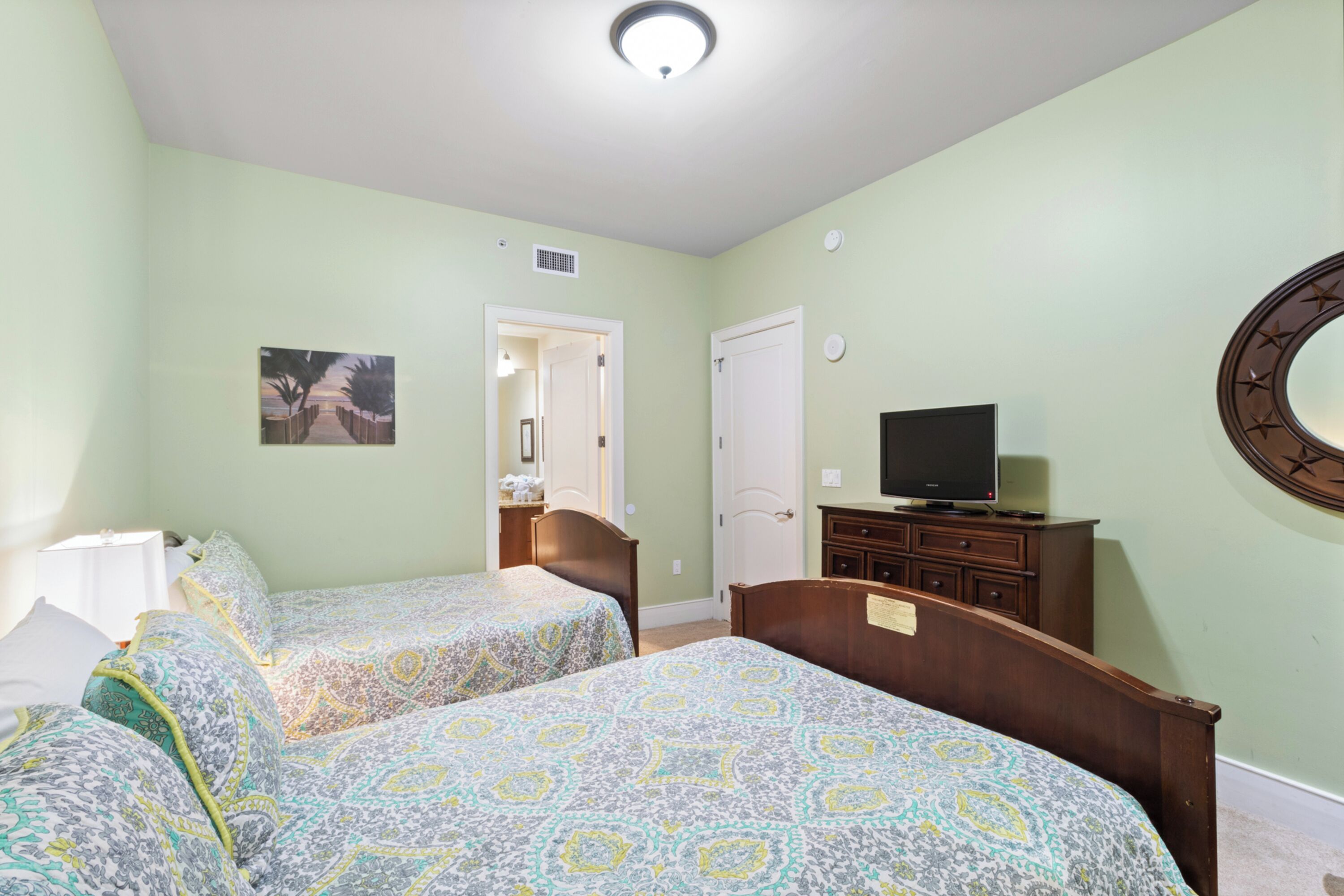 A bedroom with two beds, a dresser, a television, and a door leading to another room.