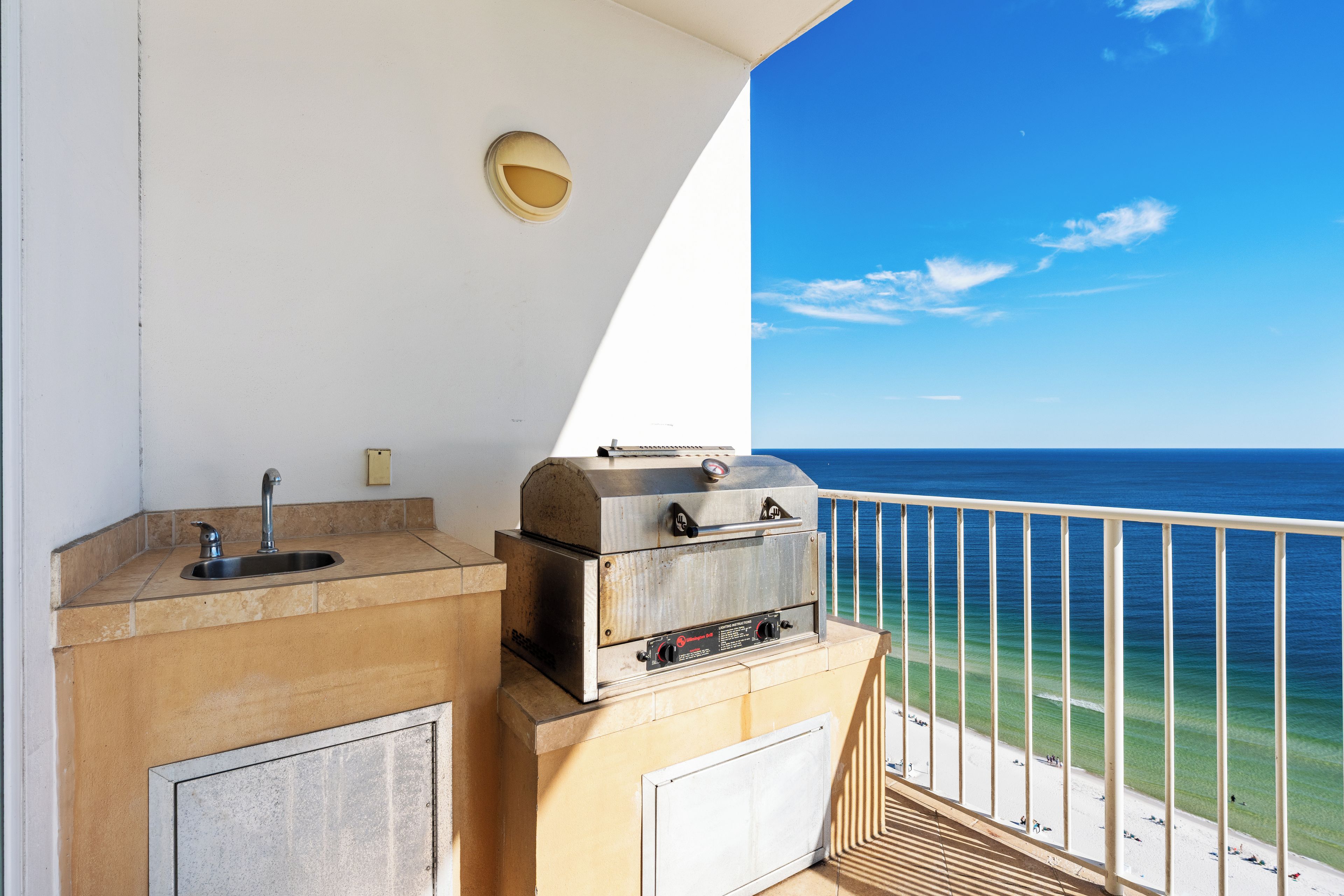 A balcony with a grill and sink, overlooking a beach.