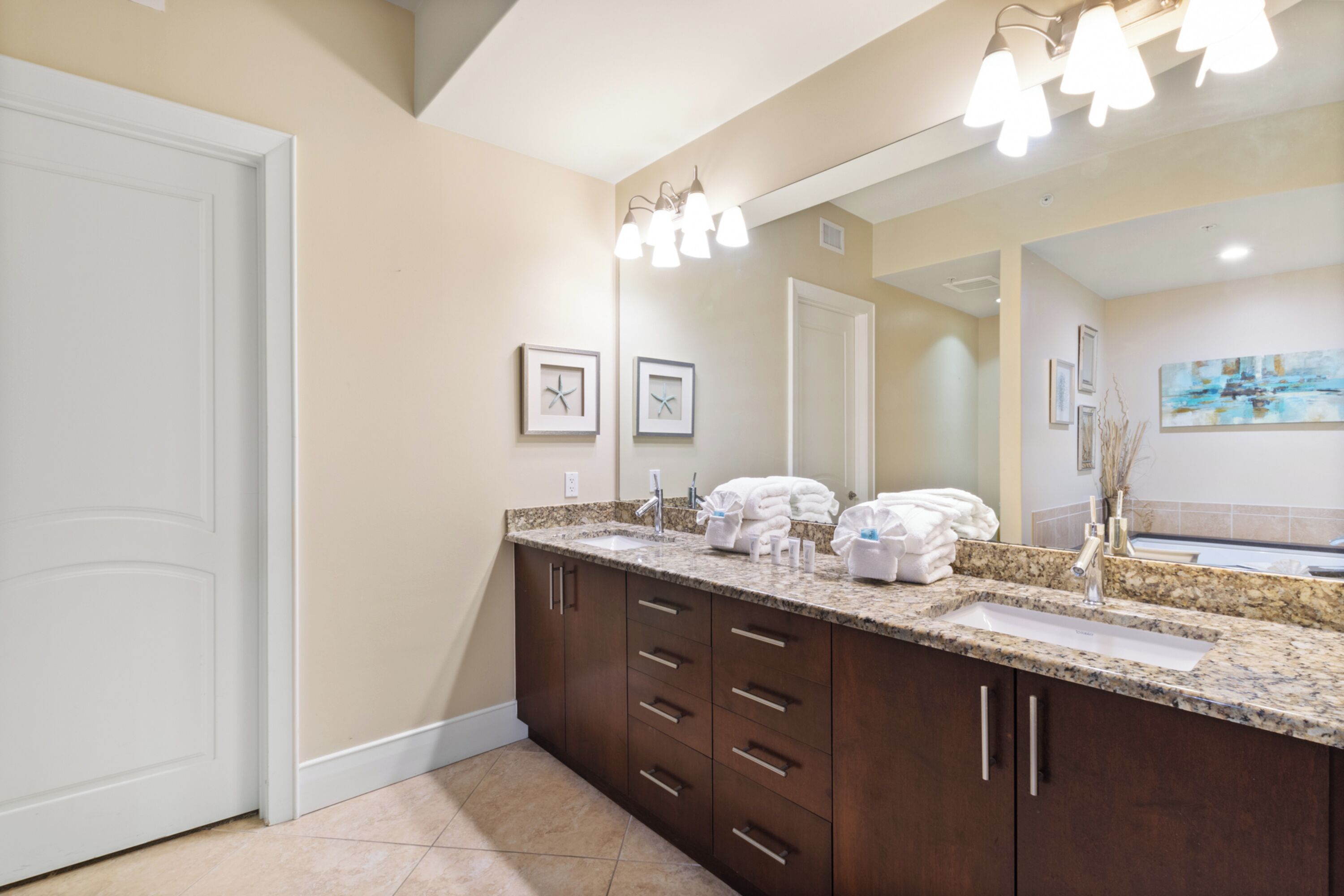 A bathroom with a large mirror, two sinks, and a vanity with drawers.