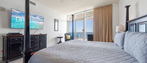 Una camera d'albergo con un letto grande, una ventola a soffitto, una TV fissata al muro e vista sull'oceano dalla finestra.