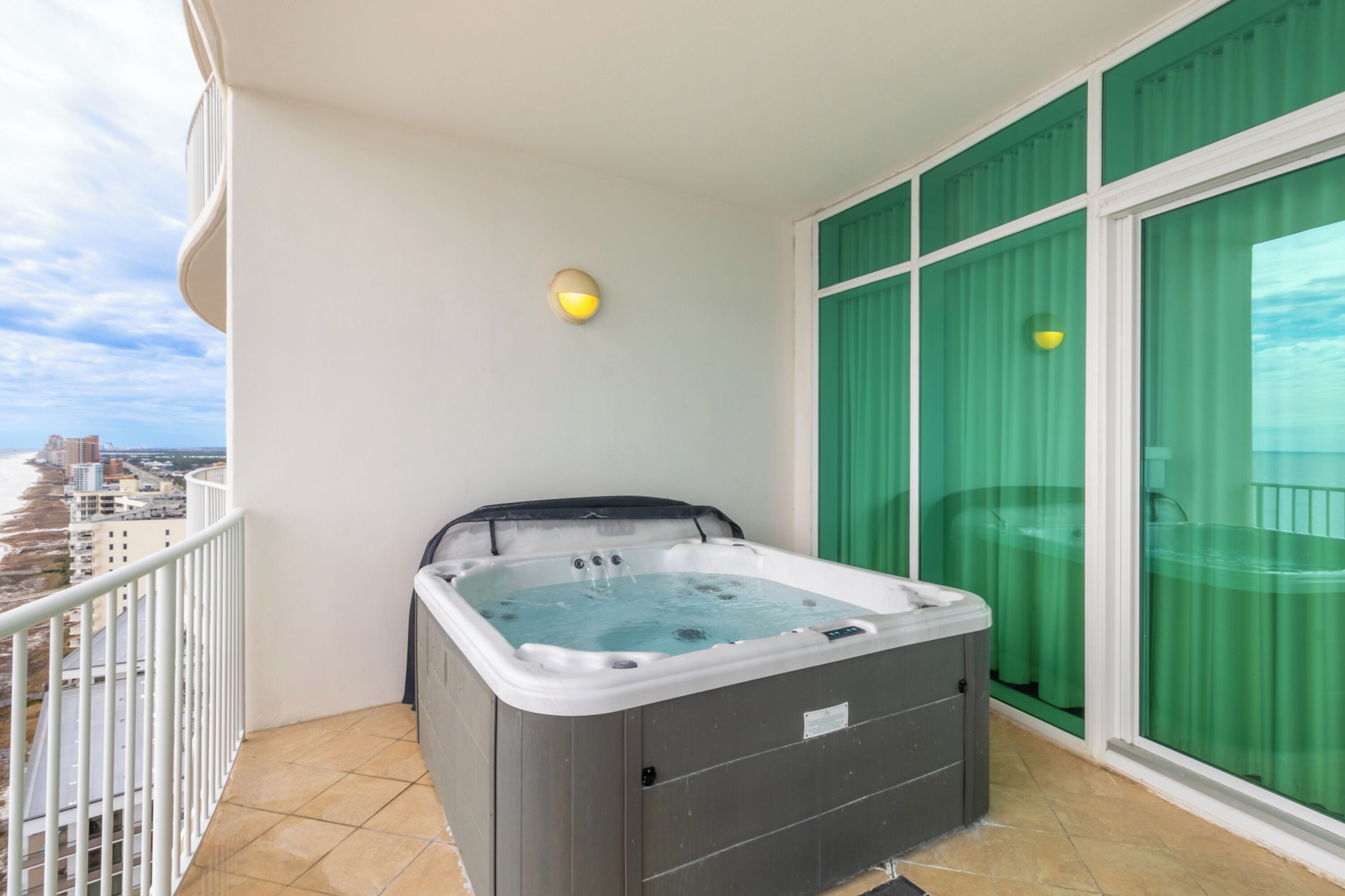 A balcony with a hot tub, a view of the city, and a green curtain.