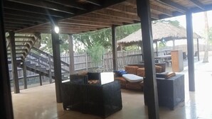 An outdoor covered patio area with wicker furniture, a staircase, and a thatched-roof structure. - Heineken Beach House  (Lagos)