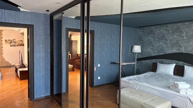 Un dormitorio moderno con una cama grande, una pared de cristal y vistas al área de estar.