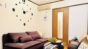 A modern living room with a brown sofa, a side table with a basket, and a wall clock. - 10 min. drive to Osaka Castle 3DK rental spacious house / capacity for 9 people (osakashi,higashinariku,kamiji)