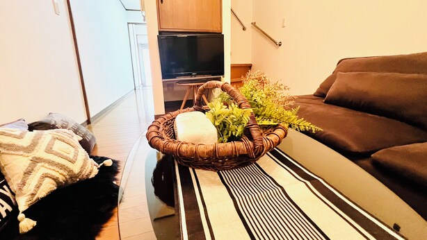 A living room with a sofa, a television, a wicker basket with plants, and a patterned rug. - 10 min. drive to Osaka Castle 3DK rental spacious house / capacity for 9 people (osakashi,higashinariku,kamiji)