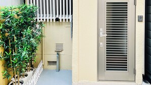 A small, beige building with a metal door and a white picket fence. There is a small table with a lamp and a potted plant. - 10 min. drive to Osaka Castle 3DK rental spacious house / capacity for 9 people (osakashi,higashinariku,kamiji)