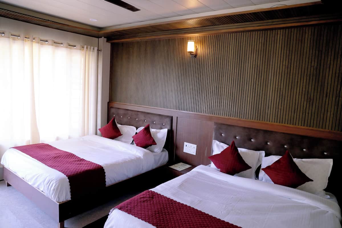 Habitación de hotel con dos camas, cada una con ropa de cama blanca y almohadas rojas, un cabecero de madera y una lámpara fijada a la pared.