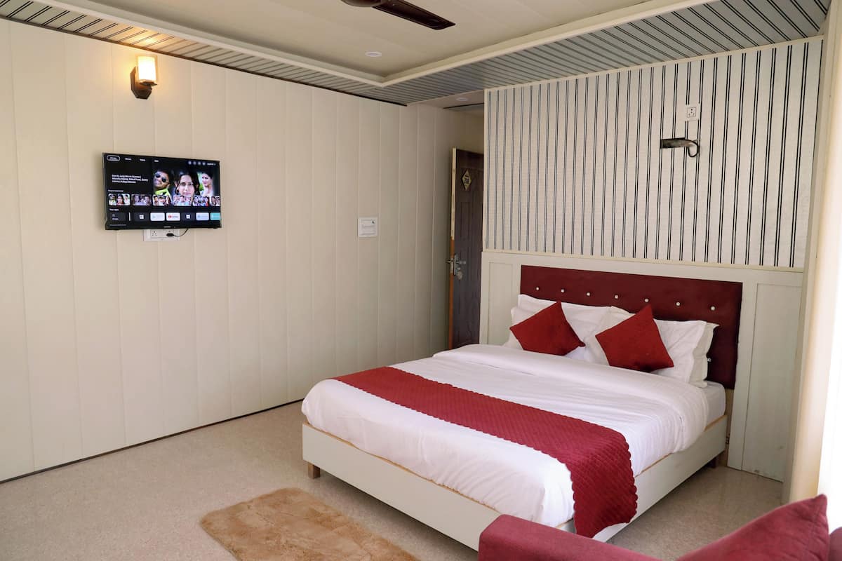 Un dormitorio ordenado con cama, televisor montado en la pared y puerta que da a otra habitación.