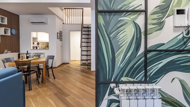 Una sala moderna con piso de madera, un área de comedor con mesa y sillas de madera, una cocina con gabinetes blancos y una escalera que sube a un nivel superior.