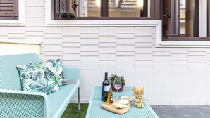 Un patio con una silla azul y una mesa dispuesta con vino, queso y galletas.
