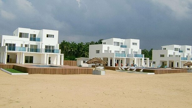 Hotel a primera línia de platja amb edificis blancs moderns, una piscina i gandules.