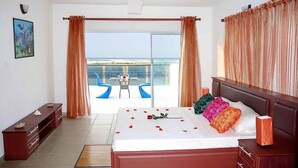 Una habitació d'hotel amb llit, una taula de nit, un taulell, un armari i una finestra amb cortines, amb vista a l'oceà.