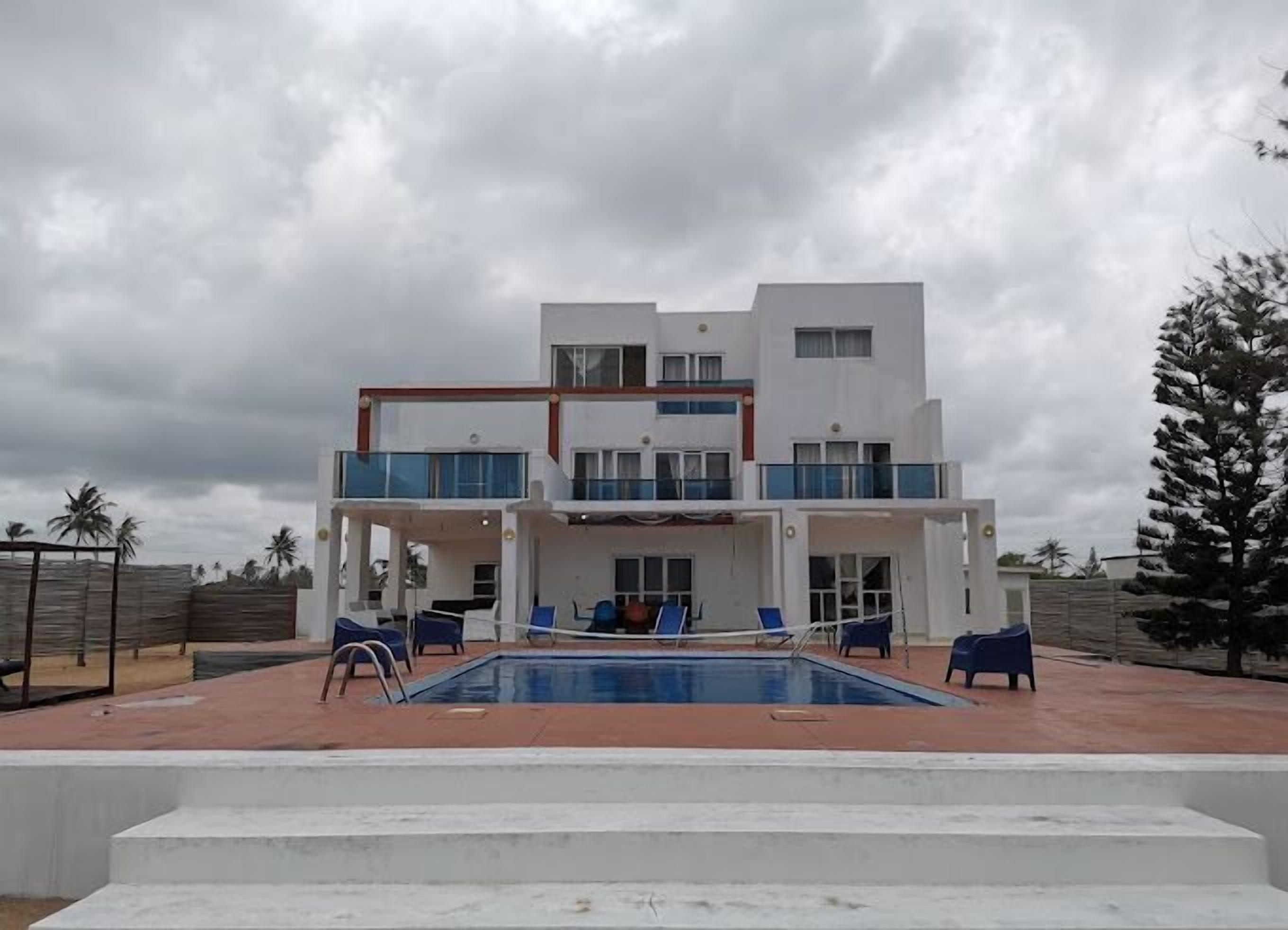 Ein modernes, zweistöckiges Gebäude mit Swimmingpool, Außenbereich und Blick auf Palmen.