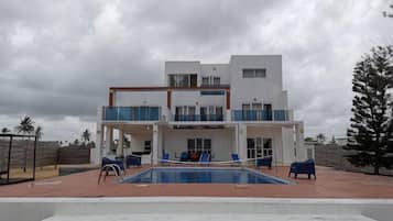 Ein modernes, zweistöckiges Gebäude mit Swimmingpool, Außenbereich und Blick auf Palmen.